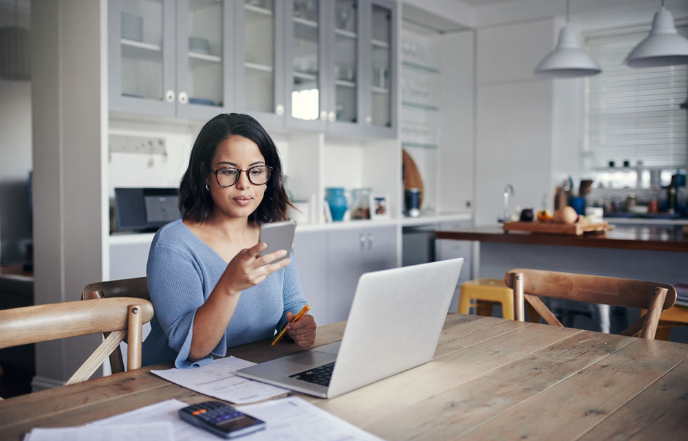 Woman sitting at kitchen table with computer and phone